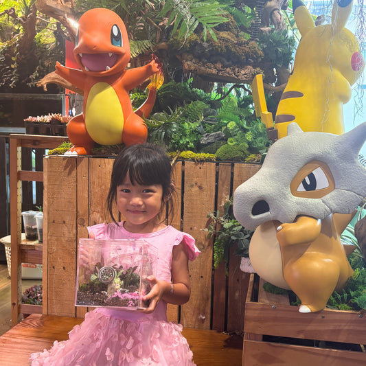 Child holding terrarium with Pokémon statues in lush green setting for kids' activities